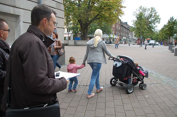 Mutter mit Kind und Kinderwagen und Mann mit Fragebogen in einer Innenstadt