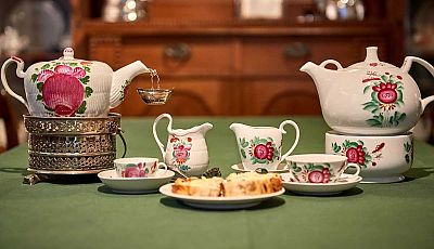 Gedeckter Tisch mit zwei Milch- und Teekannen, Teetassen und Gebäck