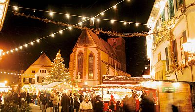 Weihnachtsmarkt im Dunkeln mit Lichterkette und Kirche im Hintergrund