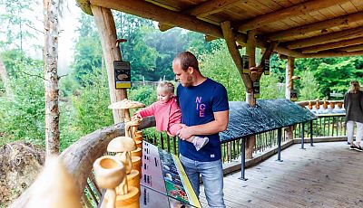 Ein Vater mit Kleinkind ertasten auf einer Holzterrasse Pilzmodelle aus Holz